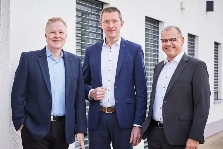 Drei Geschäftsführer von tim stehen in Anzügen vor dem Firmengebäude